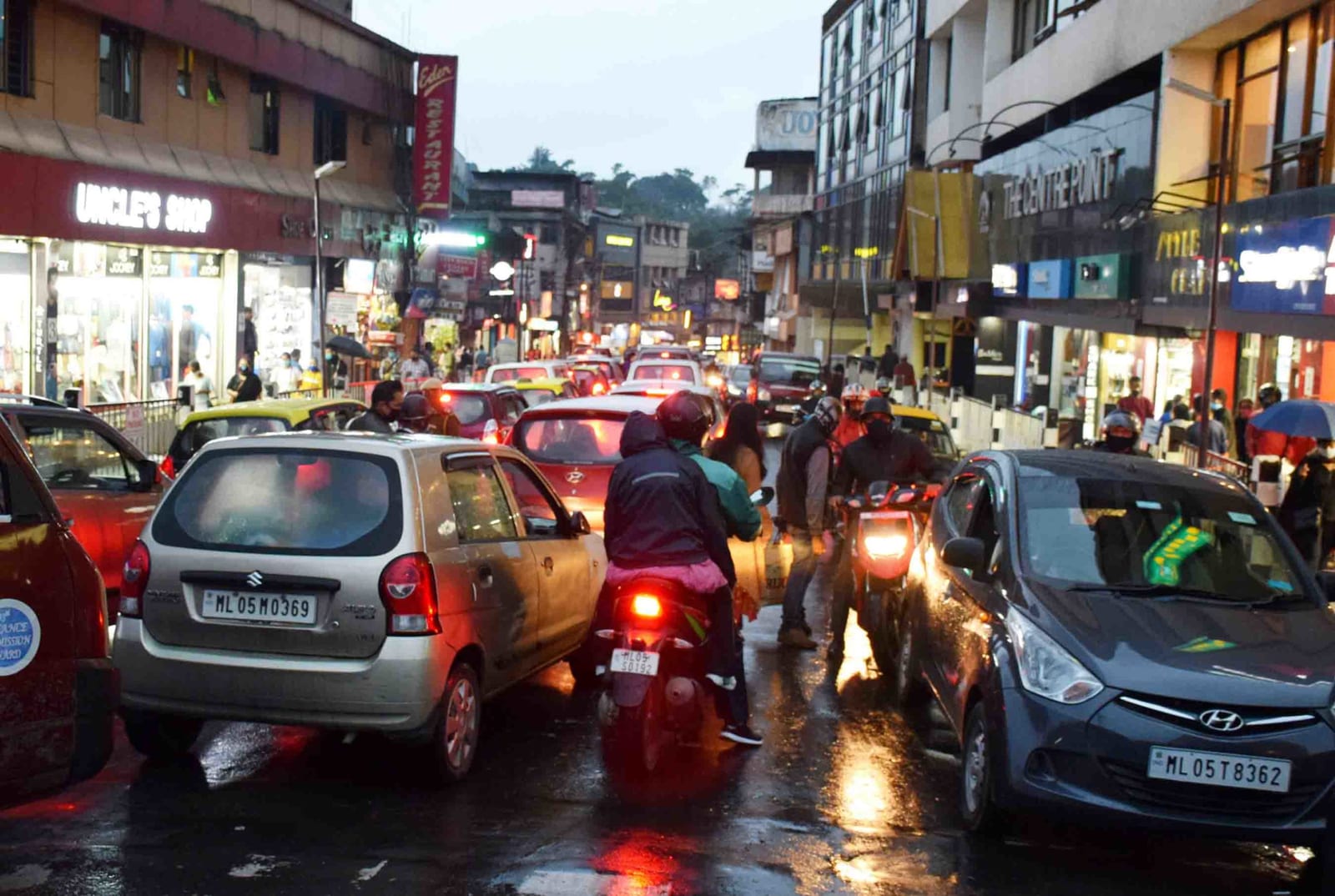 Evening peak-hour traffic in central Shillong, cars and two-wheelers queued nose to tail on a wet street lined with shopfronts